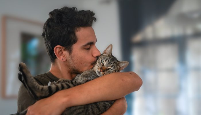 Young,Man,Holds,A,Tabby,Cat,In,His,Arms,And